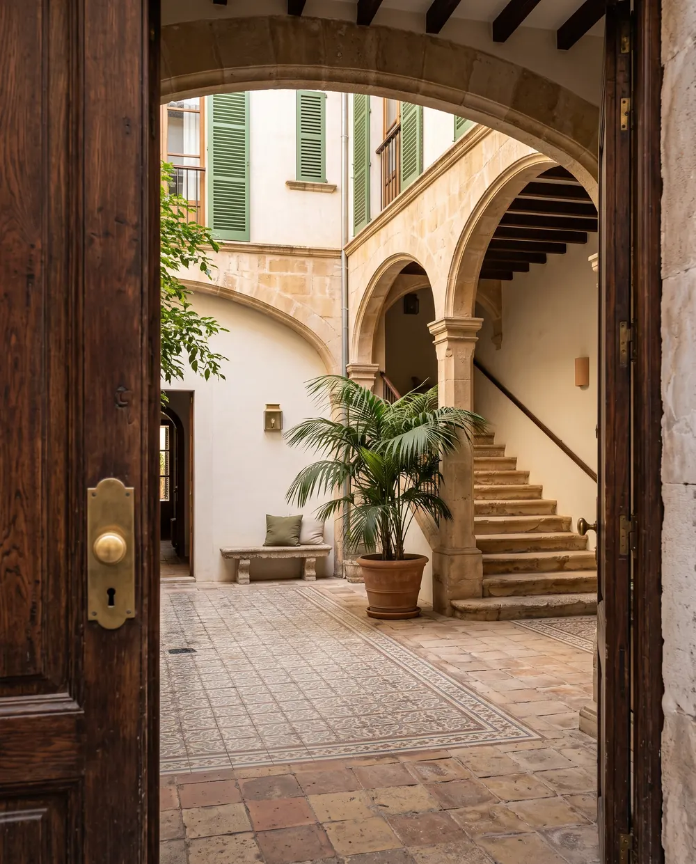 A stone patio with arches and a staircase seen through an open wooden street door