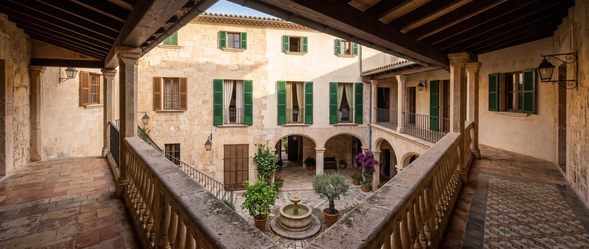 The courtyard seen from the first-floor gallery, with green shutters on the sandstone walls and potted plants around the fountain