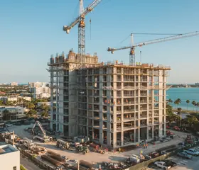 A building under construction with two cranes and its concrete frame exposed