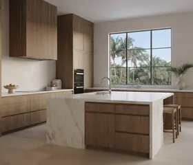 A kitchen with a marble island, wood cabinets and a window facing palm trees