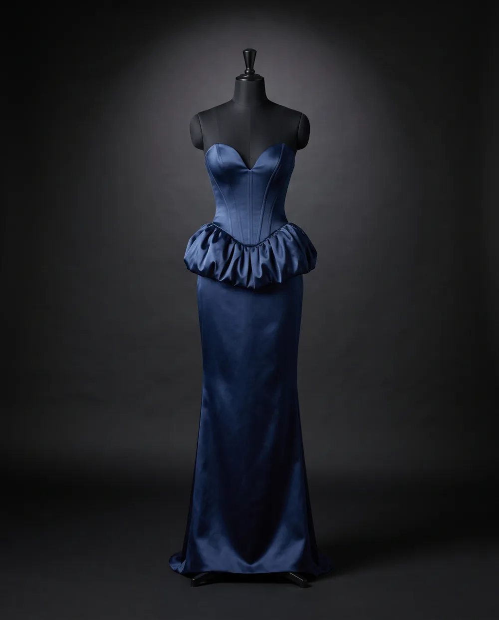 The Midnight Gown on a black dress form: a strapless midnight blue satin gown with a gathered peplum