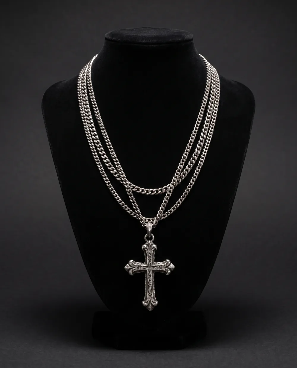 The Cross Chains on a black velvet bust: three silver chains and an engraved silver cross
