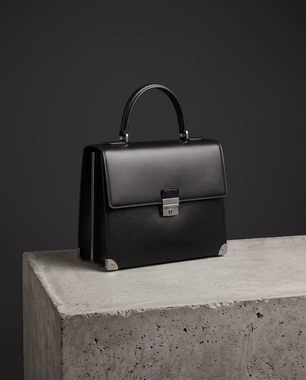 The Box Bag on a concrete block: a structured top handle bag in black leather with steel hardware