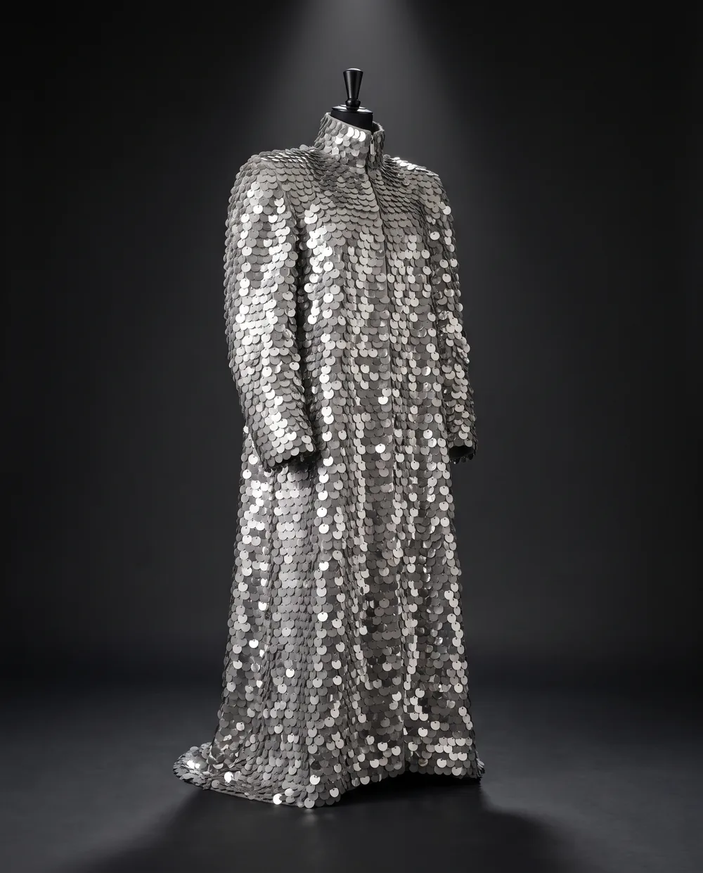 The Scale Coat on a black dress form: a floor-length coat covered in silver paillettes with a funnel collar