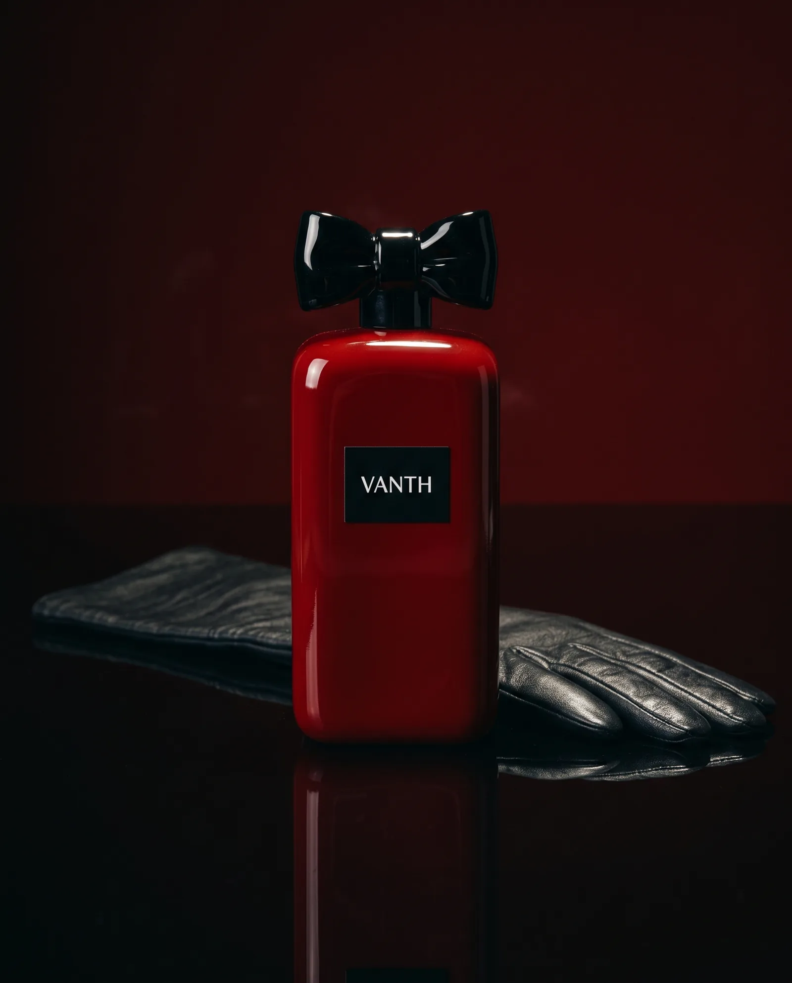 A bottle like a block of deep red lacquer with a black cap shaped like a bow, on black lacquer beside a black leather glove