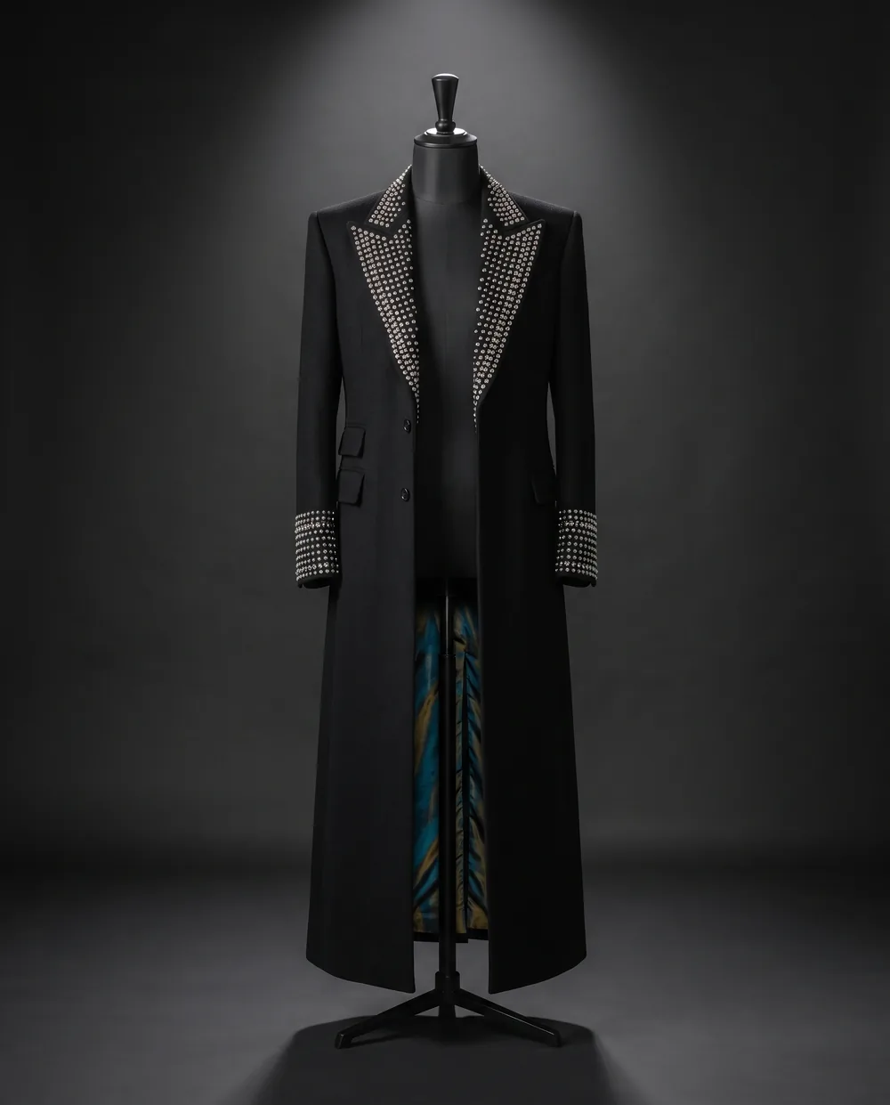 The Relay Coat on a black dress form: a long black wool coat with studded lapels and cuffs