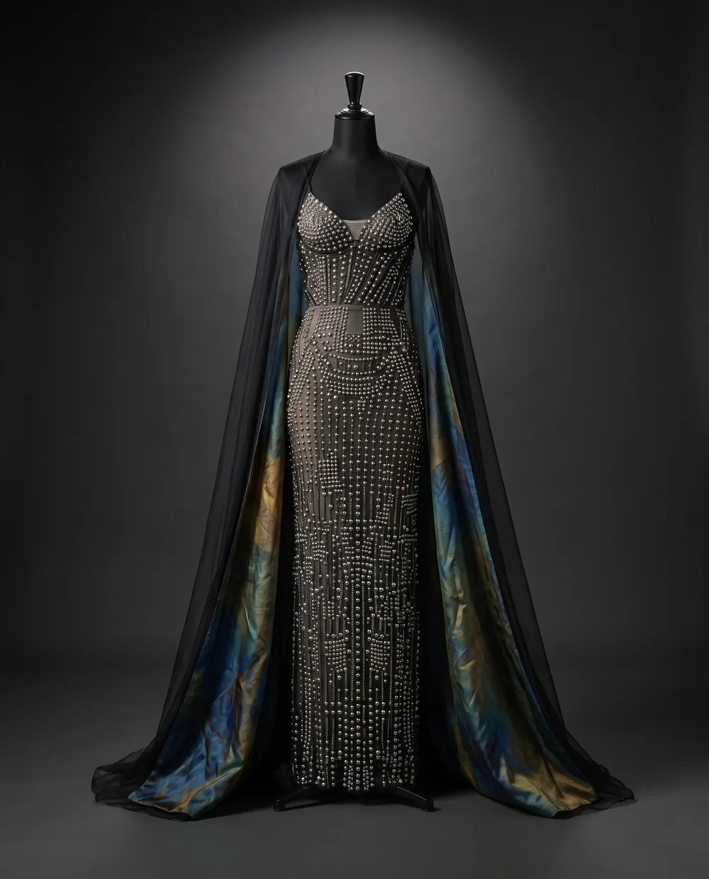 The Circuit Gown on a black dress form: a studded column gown under a sheer black cape lined in iridescent silk