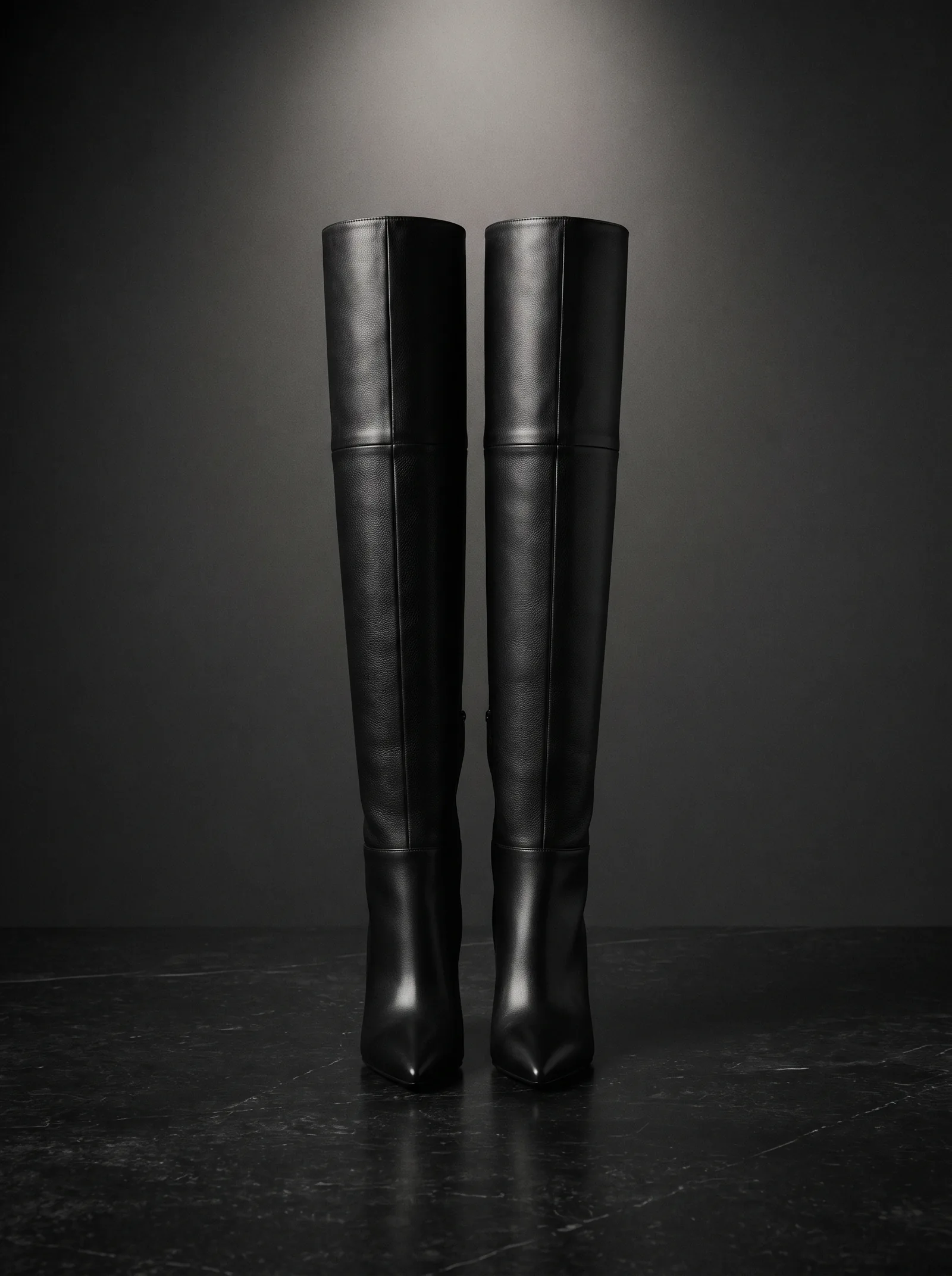 The Tall Boot: a pair of black calf leather boots that reach over the knee, with a pointed toe and a thin heel, standing on black stone