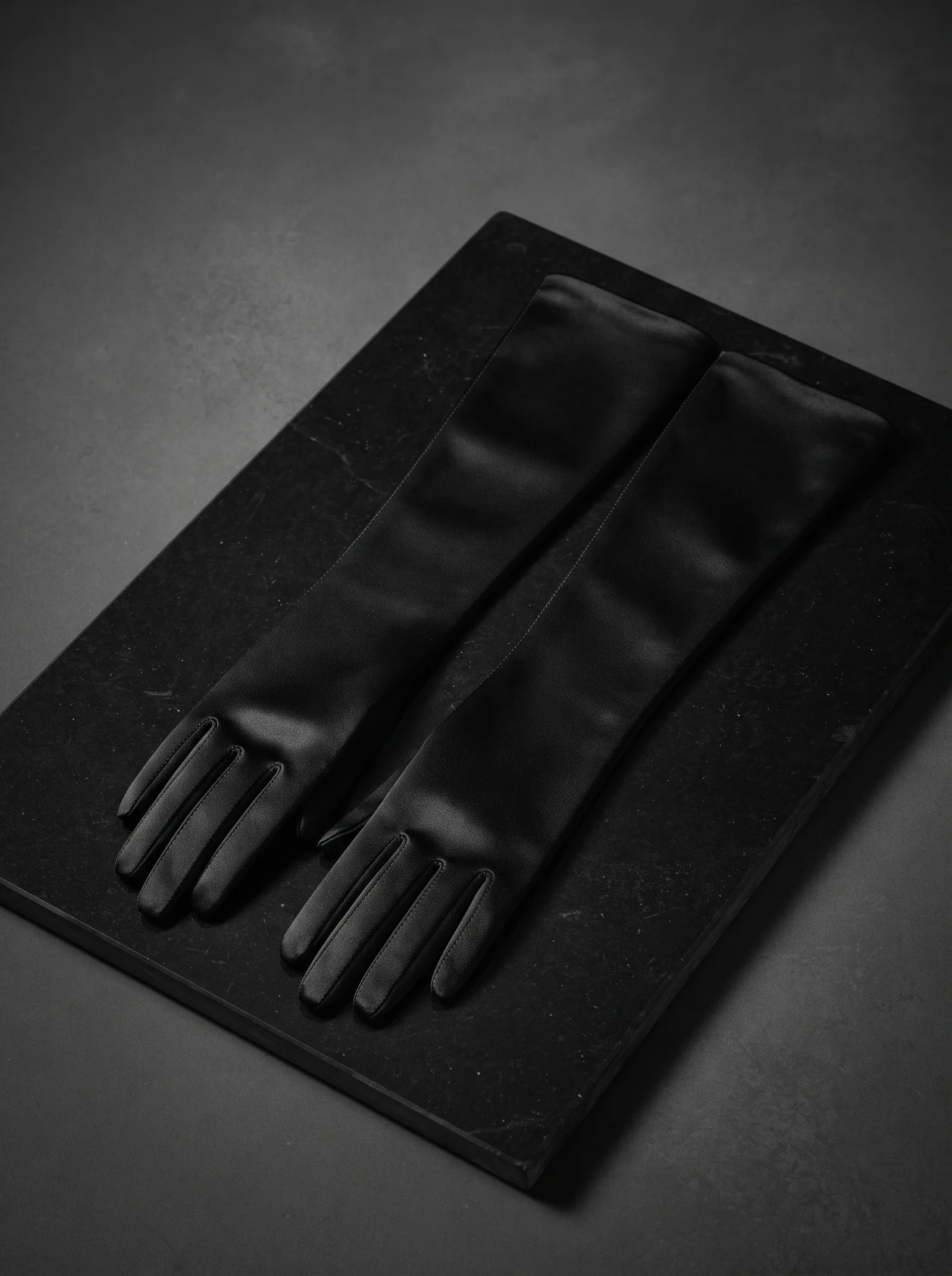 The Opera Glove: a pair of long black satin gloves laid side by side on a slab of black stone