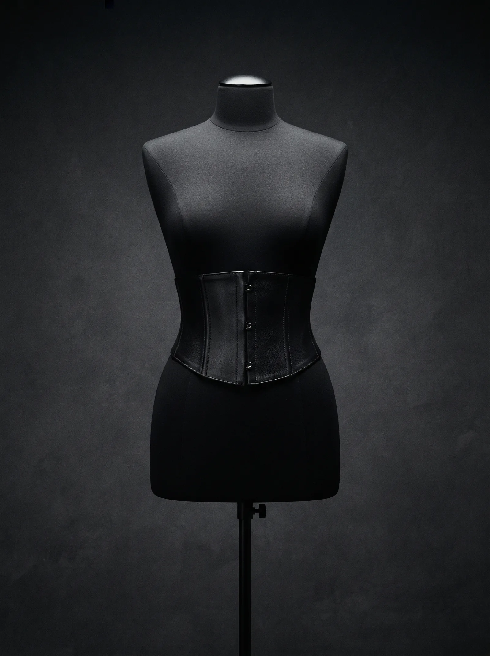 The Corset Belt on a black dress form: a wide boned belt of black leather closed at the front