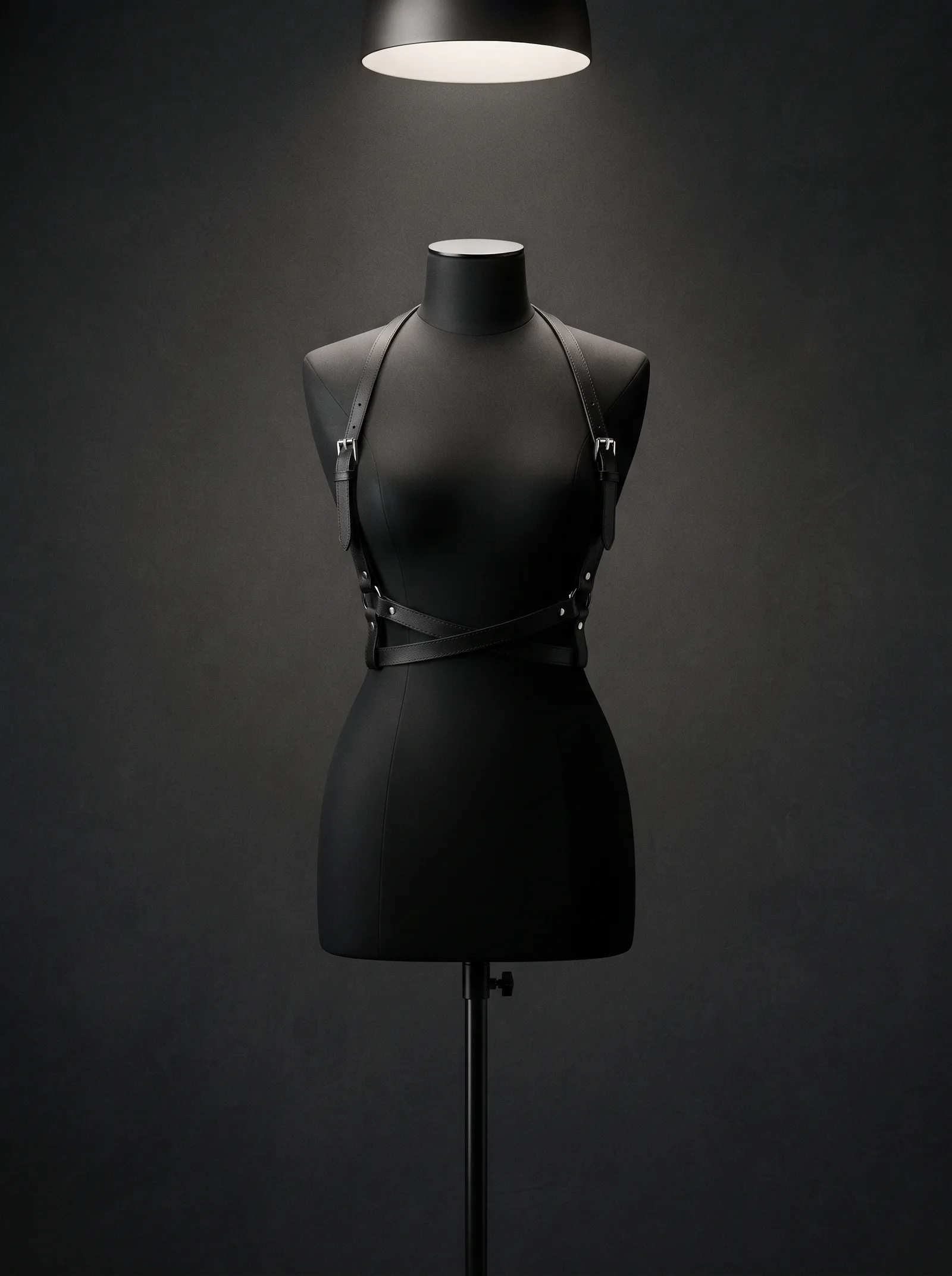 The Harness on a black dress form: black leather straps with silver buckles crossed over the chest