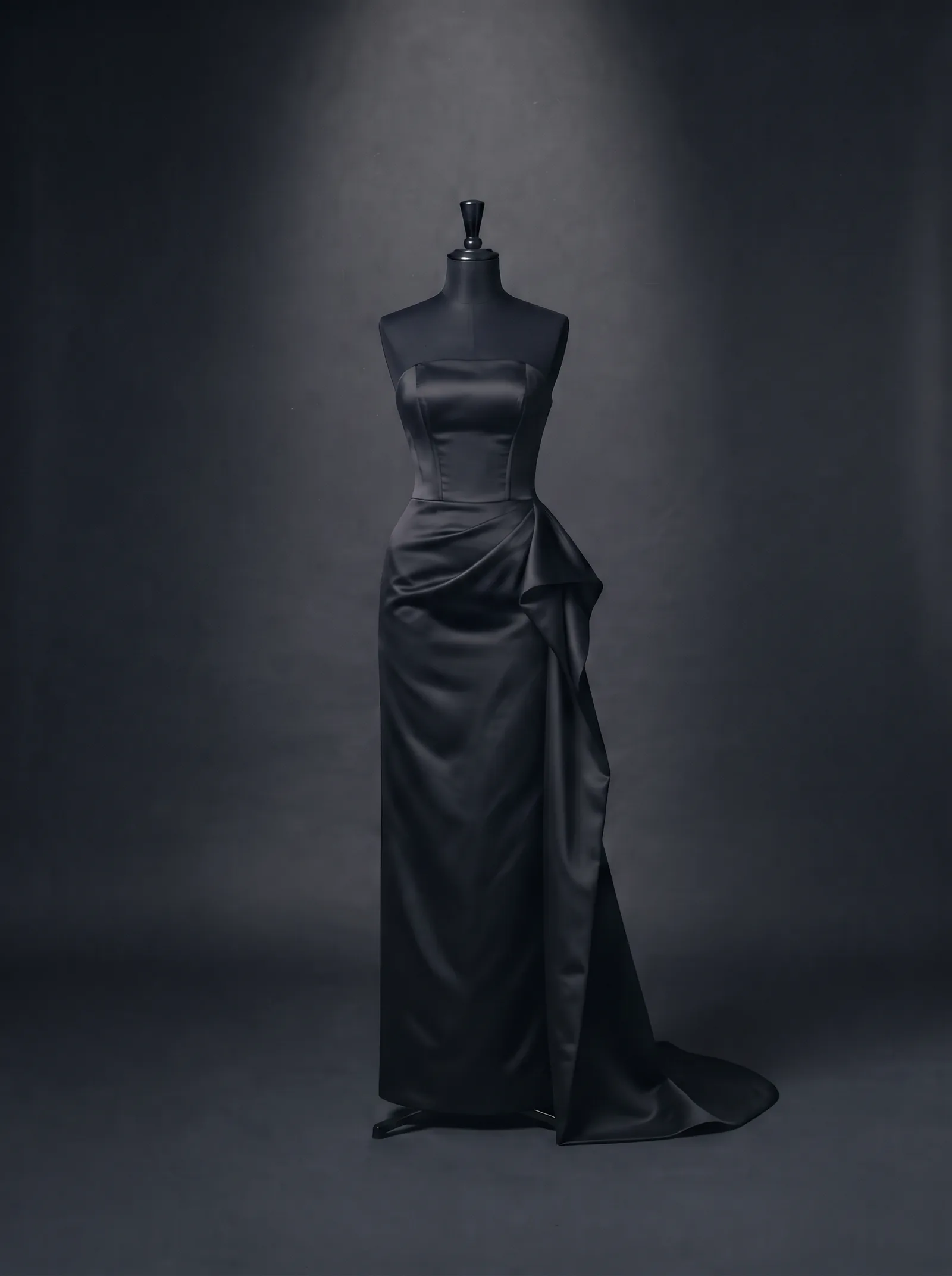 The Lacquer Gown on a black dress form: a strapless column of black duchesse satin with a fitted bodice, a drape at the hip and a short train