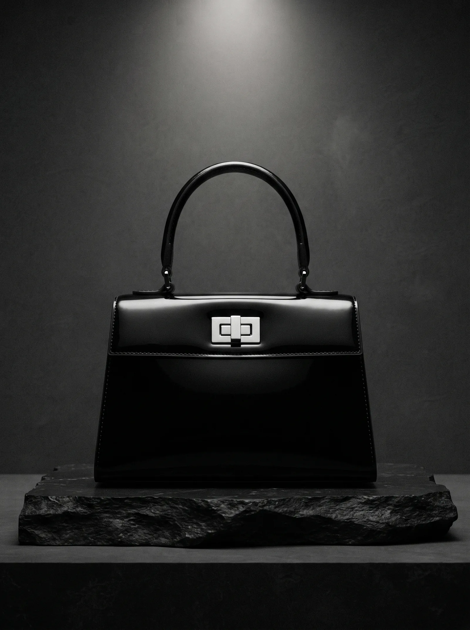 The Patent Bag on black stone: a structured handbag of black patent vinyl with one handle and a silver clasp