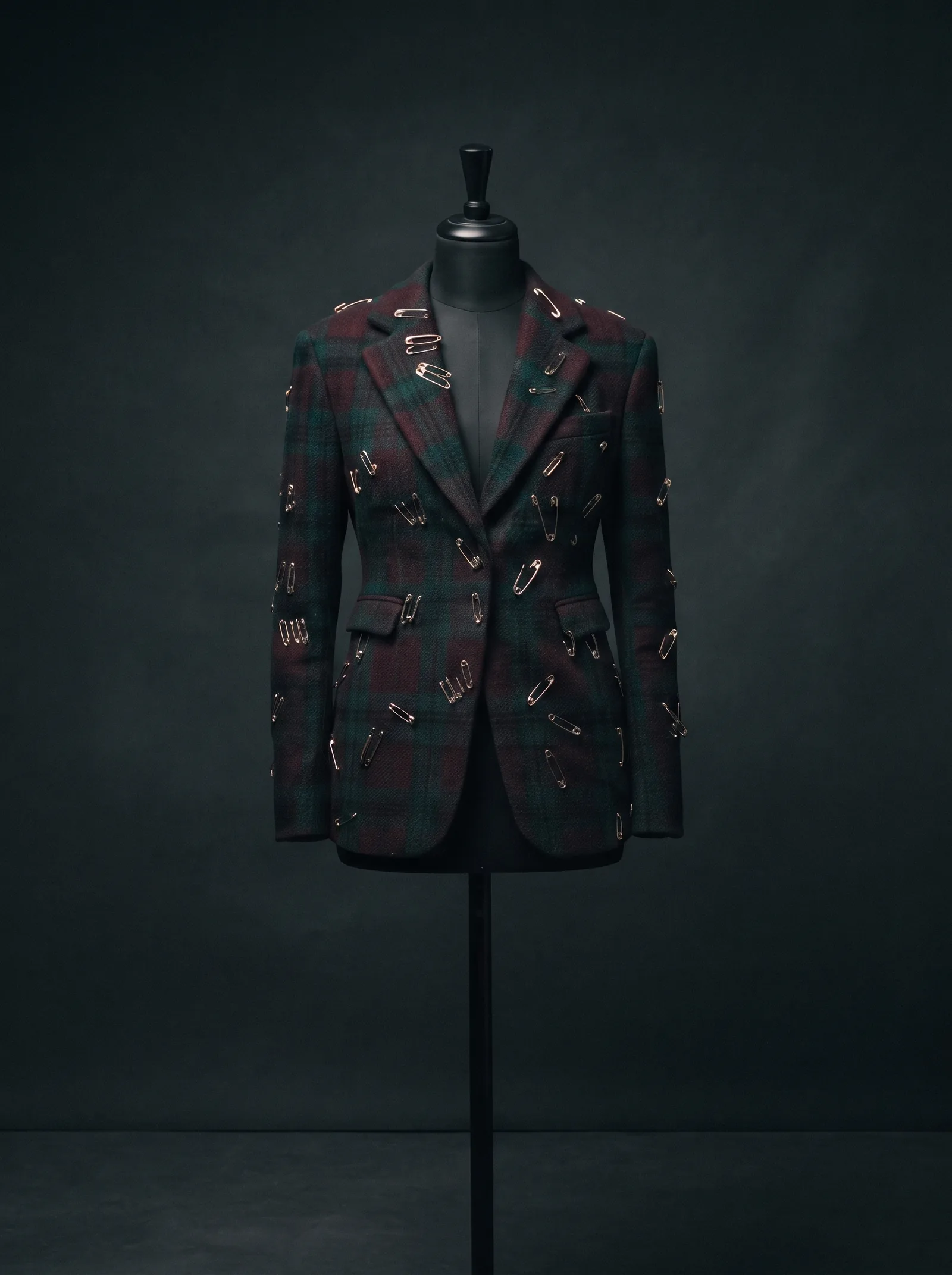 The Pinned Tartan on a black dress form: a dark green and burgundy tartan blazer pierced with silver safety pins